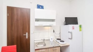 A compact kitchenette with a wooden door, a white cabinet, a black television, a refrigerator, and a red chair. - Apartments Dalamar - Studio With Terrace (Mljet)