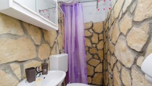 A bathroom with a stone wall, a white sink, a toilet, and a purple shower curtain. - Apartments Dalamar - Studio With Terrace (Mljet)