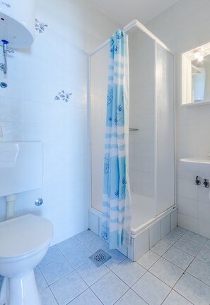 A bathroom with a toilet, a shower with a blue and white striped shower curtain, and a sink with a mirror above it. - Villa Kosa - Two Bedroom Apartment With Balcony and Sea View (Brela)