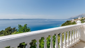 A balcony with a white balustrade overlooking a coastal view with clear blue sea and distant mountains. - Villa Kosa - Two Bedroom Apartment With Balcony and Sea View (Brela)