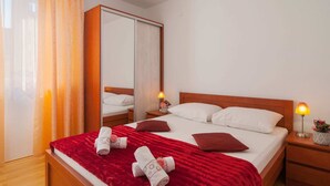 Een hotelkamer met een bed, nachtkastje, spiegel, raam met gordijnen en een rode plaid.
