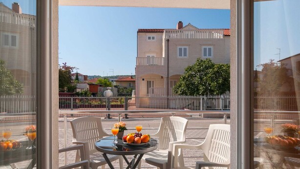 Een balkon met een tafel gedekt voor twee personen, inclusief een fruitschaal en twee glazen jus d'orange.