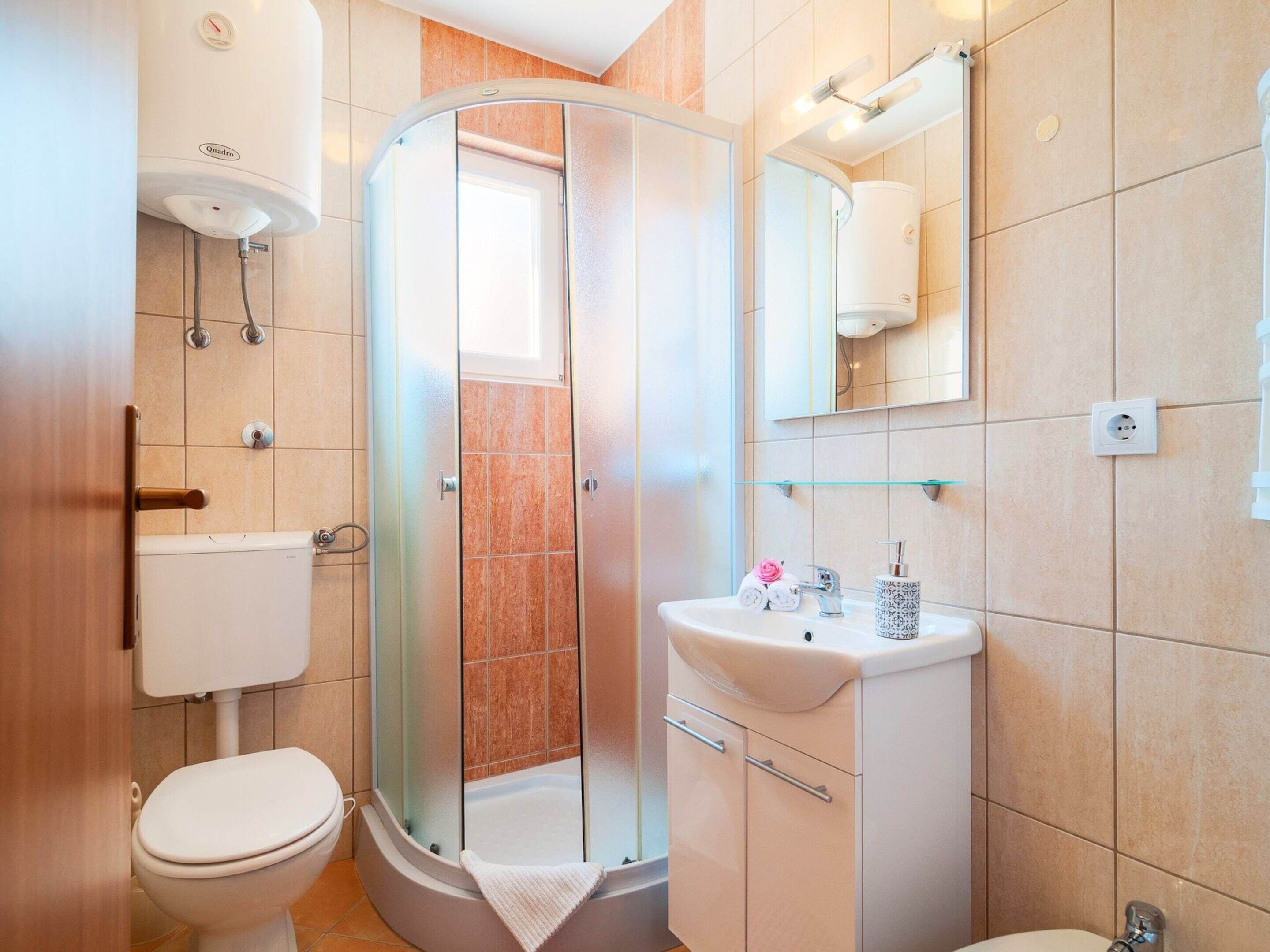 Een moderne badkamer met een glazen douchecabine, toilet, wastafel met spiegel en een handdoekrek.
