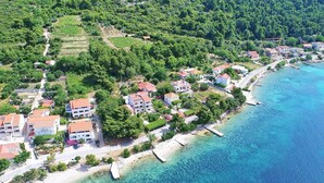 An aerial view of a coastal village with houses along the shoreline, clear blue waters, and lush greenery. - Apartments Marko Peljesac - Two Bedroom Apartment With Balcony (Orebic)