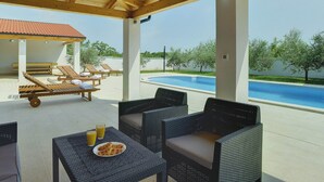 A covered outdoor area with a pool, lounge chairs, and a table with croissants and juice. - Family Villa With Swimming Pool (Liznjan)