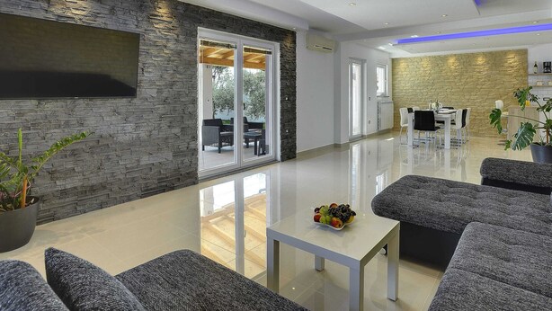 A spacious living area with a modern design, featuring a stone wall, a flat-screen TV, and a dining area with a table and chairs. - Family Villa With Swimming Pool (Liznjan)