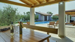 A wooden table with a bottle and glasses, a pool, lounge chairs, and a covered patio area. - Family Villa With Swimming Pool (Liznjan)
