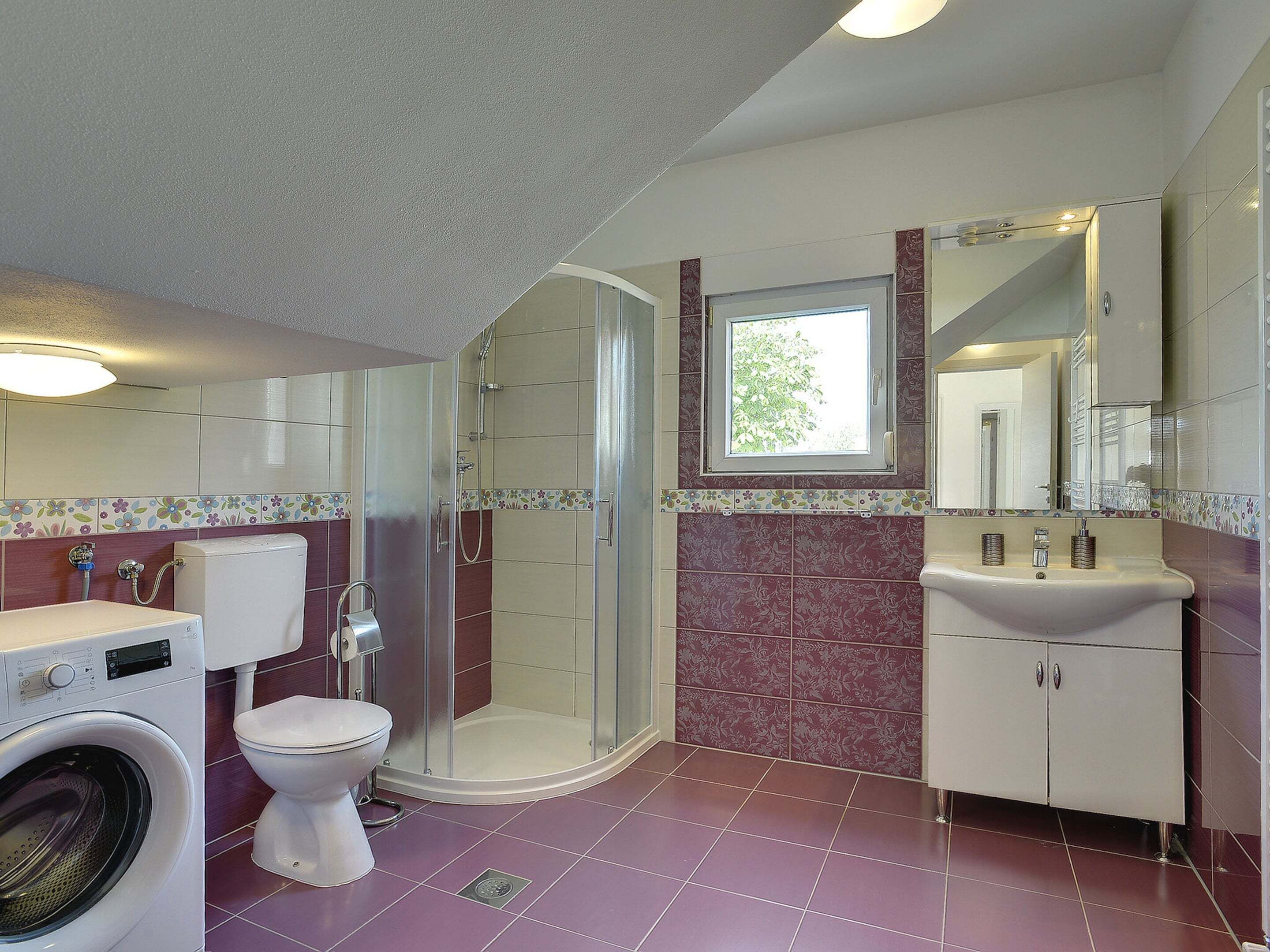 A bathroom with a washing machine, toilet, shower, and sink.