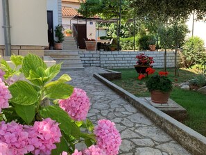 A stone pathway leading to a building entrance, surrounded by potted plants and flowers. - Apartment With one Room Near City Centre (Pula)