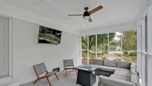 Un ambiente soleado con ventilador de techo, televisor montado en la pared y un gran ventanal con vistas al exterior.