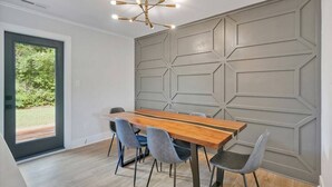 Un comedor moderno con una mesa de madera y sillas grises tapizadas, un panel mural geométrico y una lámpara de techo.
