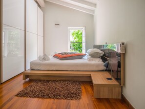 A modern bedroom with a bed, a bedside table, a mirror, and a view of greenery outside. - Belvilla by OYO Casa Dana (Sale Marasino)