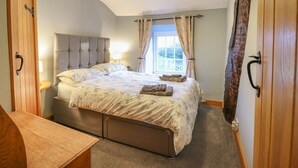 A bedroom with a bed, bedside tables, a wooden dresser, and a window with curtains. - Ynys (Dyffryn Ardudwy)