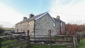 A stone house with a sloped roof and a wooden fence in front. - Ynys (Dyffryn Ardudwy)