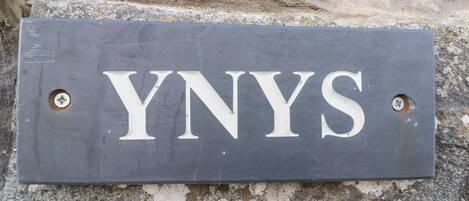 Un letrero de pizarra oscuro con las letras 'YNYS' montadas sobre una superficie de piedra.