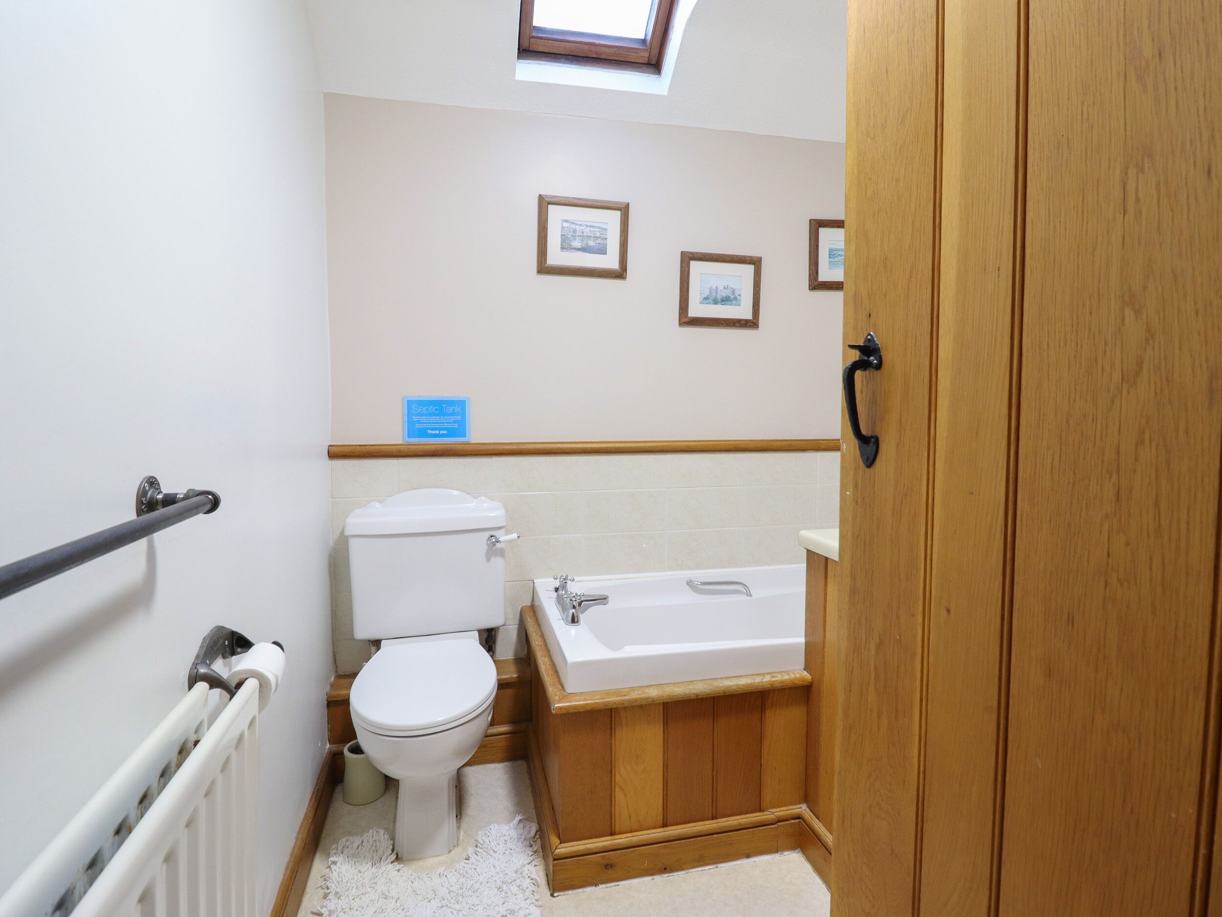 A bathroom with a toilet, bathtub, wooden vanity, and a skylight.