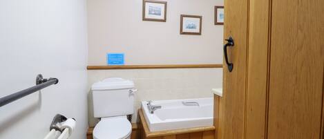 A bathroom with a toilet, bathtub, wooden vanity, and a skylight.