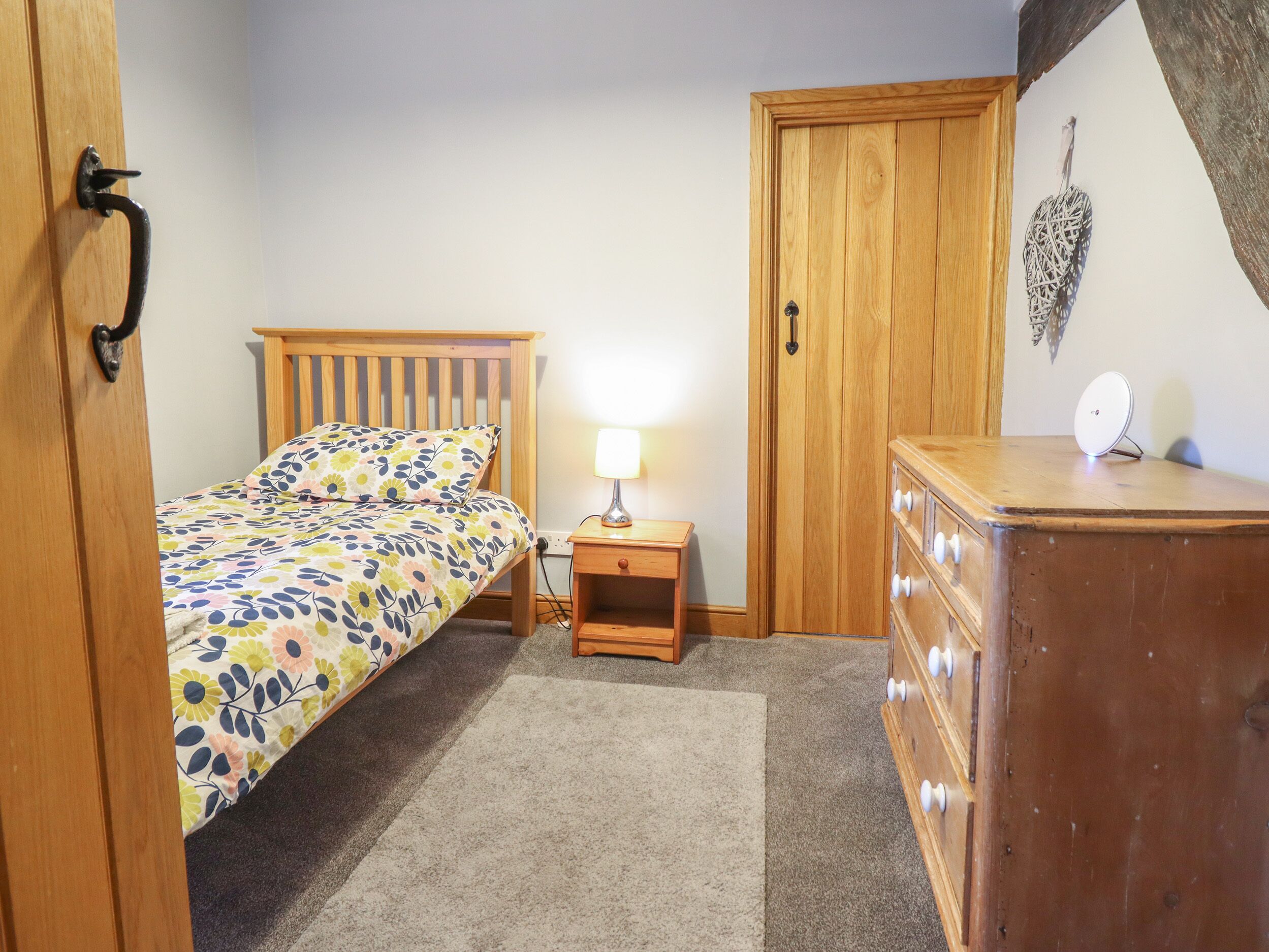 A bedroom with a wooden bed, a nightstand with a lamp, a dresser, and a door.