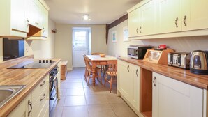 A kitchen with wooden cabinets, a dining table, chairs, a microwave, a toaster, and a kettle. - Ynys (Dyffryn Ardudwy)