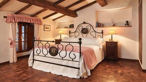 A bedroom with a wooden ceiling, a bed with a metal frame, a window with curtains, and a bedside table with a lamp.
