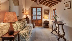 A cozy room with a wooden ceiling, a floral sofa, a wooden table, and a door with frosted glass panels. - Charming House in Tuscany With Pool (Umbertide)