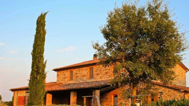 A stone building with a tiled roof, a large tree in front, and a stone pathway leading to the entrance. - Belvilla by OYO Vocabolo Ronda3 12 p (Parrano)