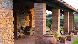 A covered outdoor seating area with stone walls, brick pillars, wicker furniture, and potted plants. - Belvilla by OYO Vocabolo Ronda3 12 p (Parrano)