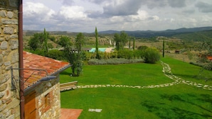 A stone building with a tiled roof overlooking a well-maintained lawn and a distant view of hills and a swimming pool. - Belvilla by OYO Vocabolo Ronda3 12 p (Parrano)