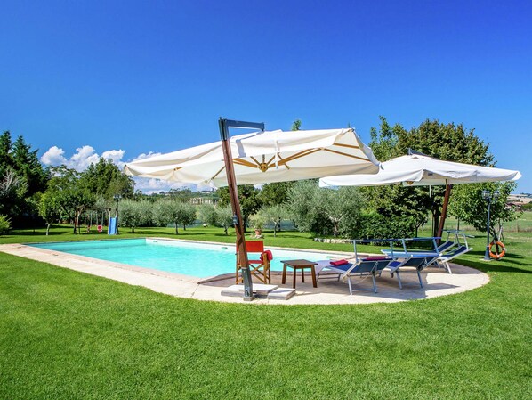 A swimming pool with lounge chairs and umbrellas, surrounded by well-maintained grass and trees.