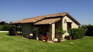 A stone house with a tiled roof, surrounded by a well-maintained lawn and various potted plants. - Belvilla by OYO Da Pino Bilocale (Marsciano)