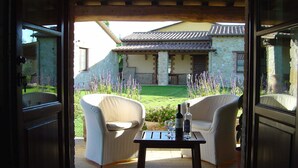 An open patio with two white armchairs and a table, a stone building in the background, and purple flowers in the garden. - Belvilla by OYO Da Pino Bilocale (Marsciano)