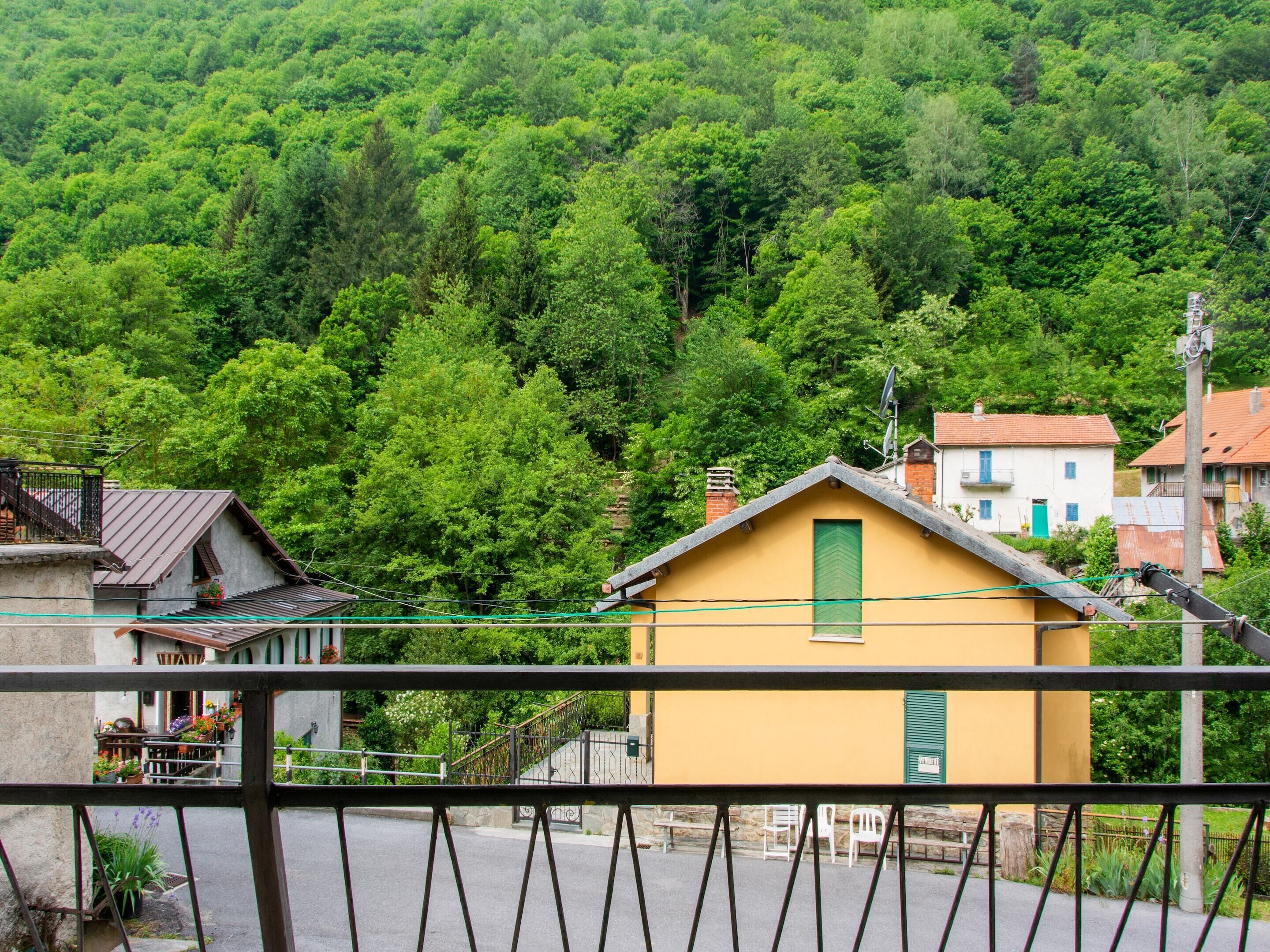 Un bâtiment jaune avec une porte verte, entouré d’arbres verdoyants et situé au pied d’une colline.