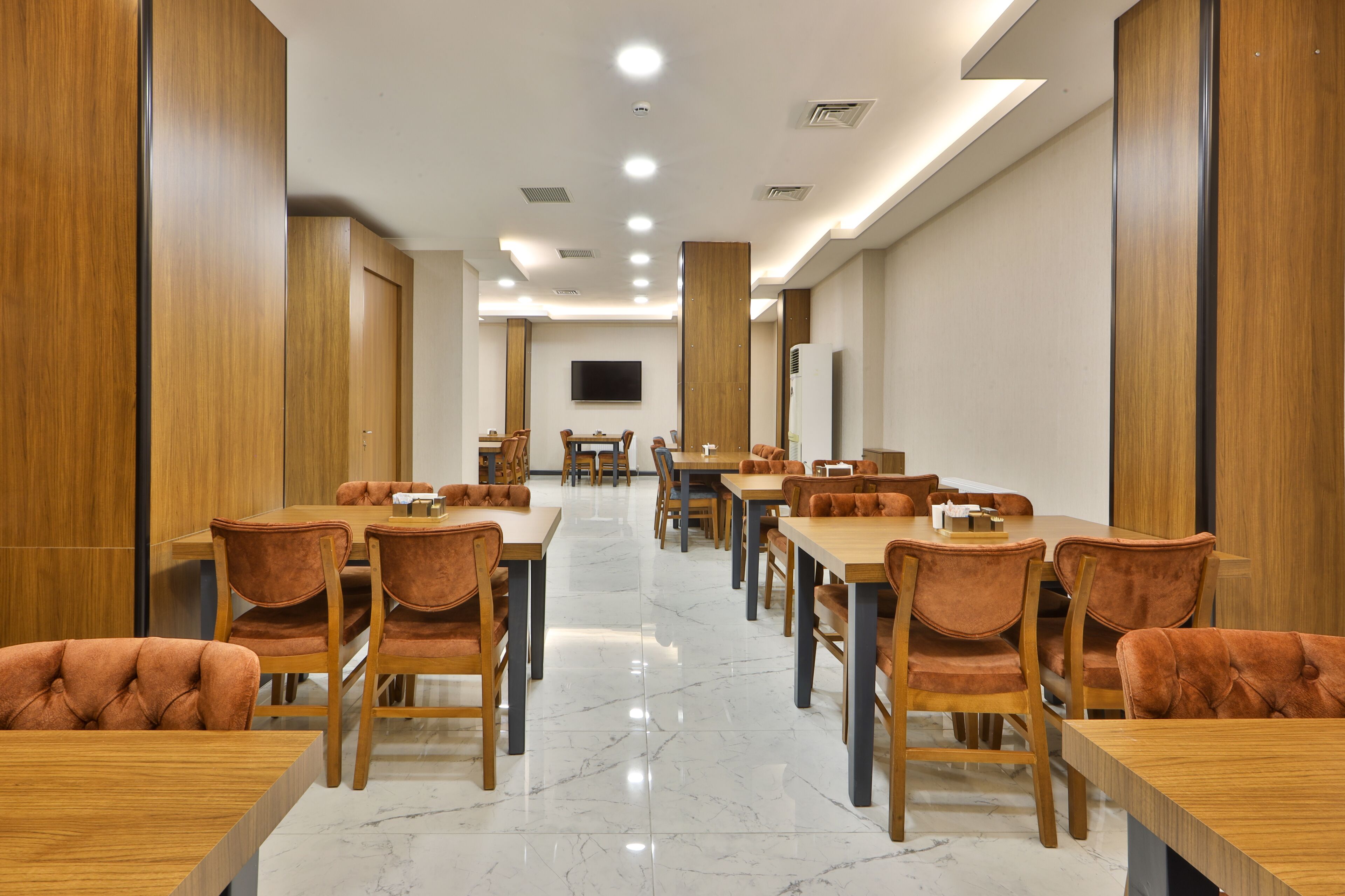 A conference room with multiple tables and chairs, a flat-screen TV, and a marble floor.