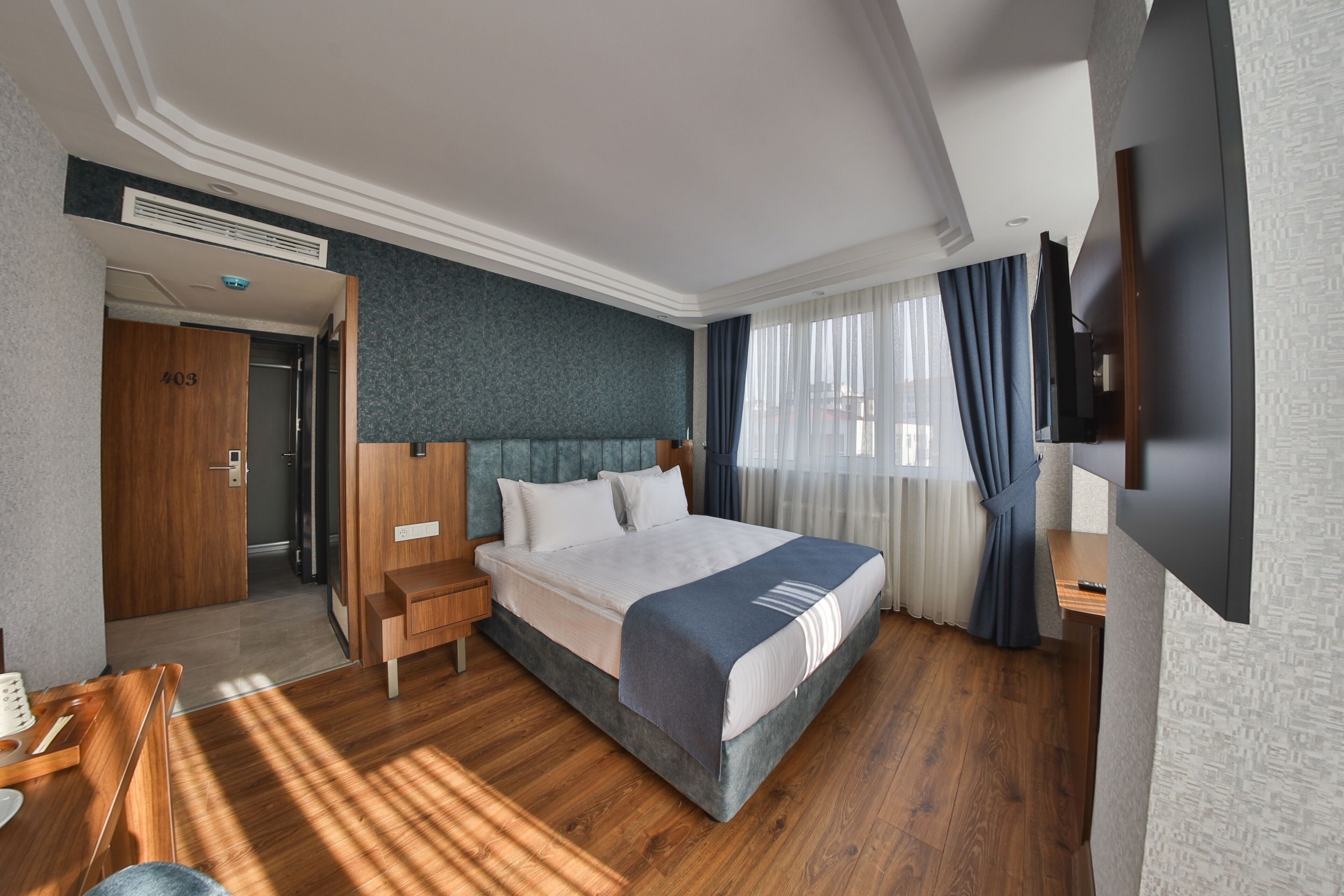 A modern hotel room with a large bed, wooden flooring, a flat-screen TV, and a desk with a chair.