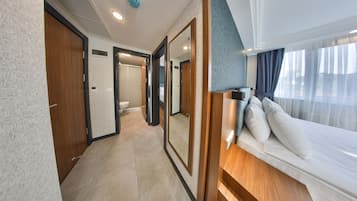A modern hotel room with a large bed, a wooden headboard, and a view of the outdoors through a window.