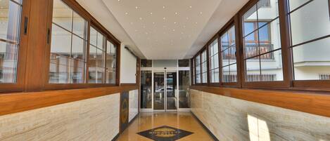 A hallway with wooden paneling, large windows, and a patterned floor leading to a door.