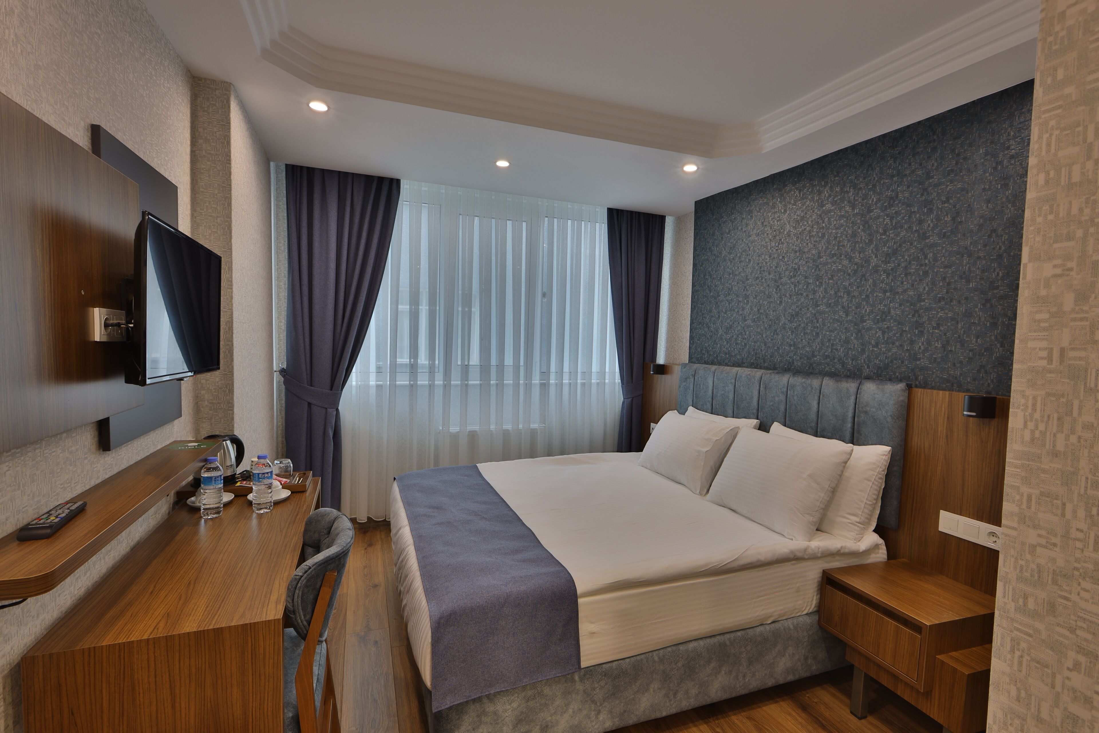 Una habitación de hotel moderna con una cama grande, un escritorio con una silla, un televisor y una ventana con cortinas.