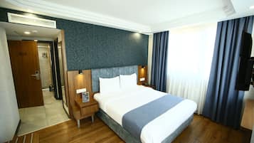Habitación de hotel con una cama grande, suelo de madera, una pared oscura y un televisor a la derecha.