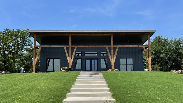A modern building with a dark facade, large windows, and a wooden structure on top.