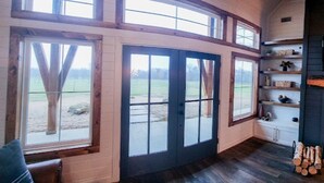 A room with large windows, wooden beams, and a built-in shelf with items.