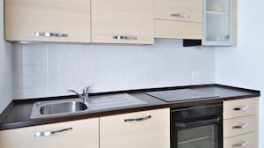 A modern kitchen with light wood cabinets, a stainless steel sink, a black oven, and a glass-fronted cabinet. - Apartment by Lake Como Near Spiaggia di Dervio (Dervio)