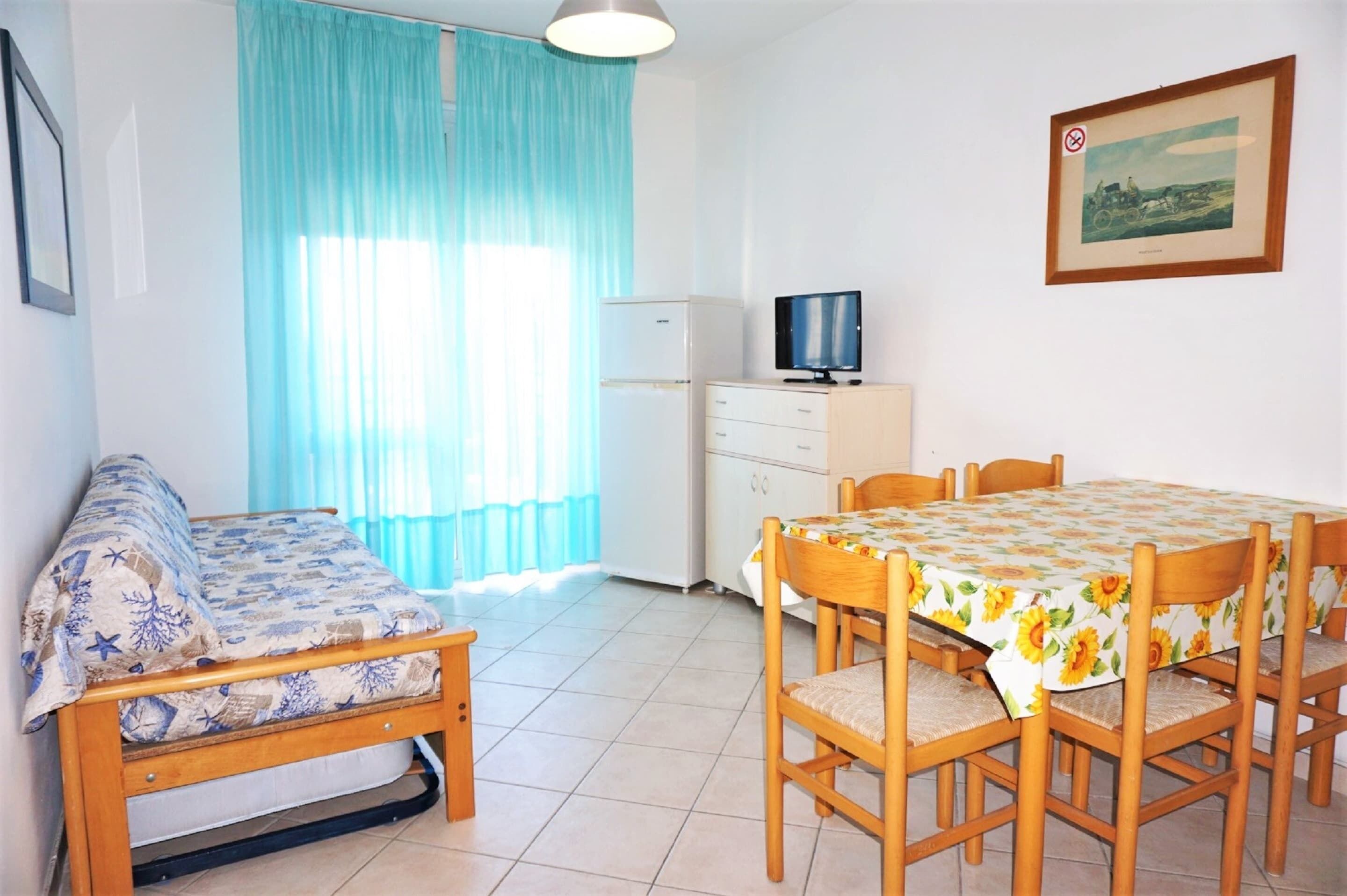 A room with a bed, a small table, a TV, and a dining table with chairs.