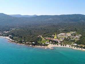 An aerial view of a coastal town with a beach, houses, and a forested hill in the background. - Apartments Lemes - Comfort One Bedroom Apartment With Garden View (Janjina)