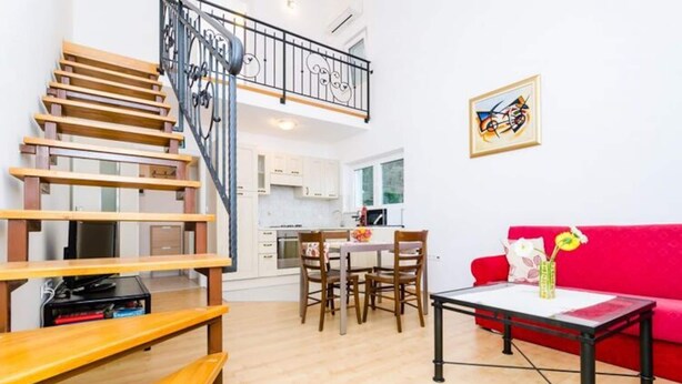 A modern apartment with a wooden staircase, a dining area, a red sofa, and a kitchen in the background. - Apartments Nikola - Superior One Bedroom Apartment With Sea View (Dubrovnik)