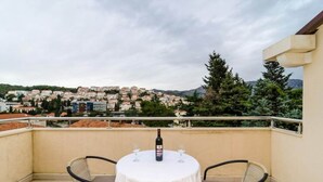 A balcony with a table and chairs, a bottle of wine, and a view of a town. - Apartments Nikola - Superior One Bedroom Apartment With Sea View (Dubrovnik)