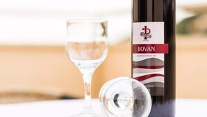 A bottle of Bovan wine and an empty wine glass on a table. - Apartments Nikola - Superior One Bedroom Apartment With Sea View (Dubrovnik)