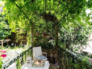 Eine Garten-Terrasse mit einem weißen Esstisch, umgeben von üppiger Bepflanzung und einer Steinmauer.