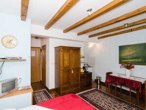 Ein Zimmer mit Holzbalken, einem Schrank aus Holz, einem Esstisch mit roter Tischdecke, einer Uhr und einem Bild an der Wand.