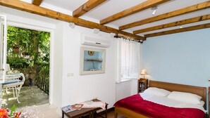 A bedroom with a wooden ceiling, a bed with a red blanket, a bedside table, a mirror, and a window with curtains. - Apartment Taura - Studio Apartment With Balcony and Old City View (Dubrovnik)