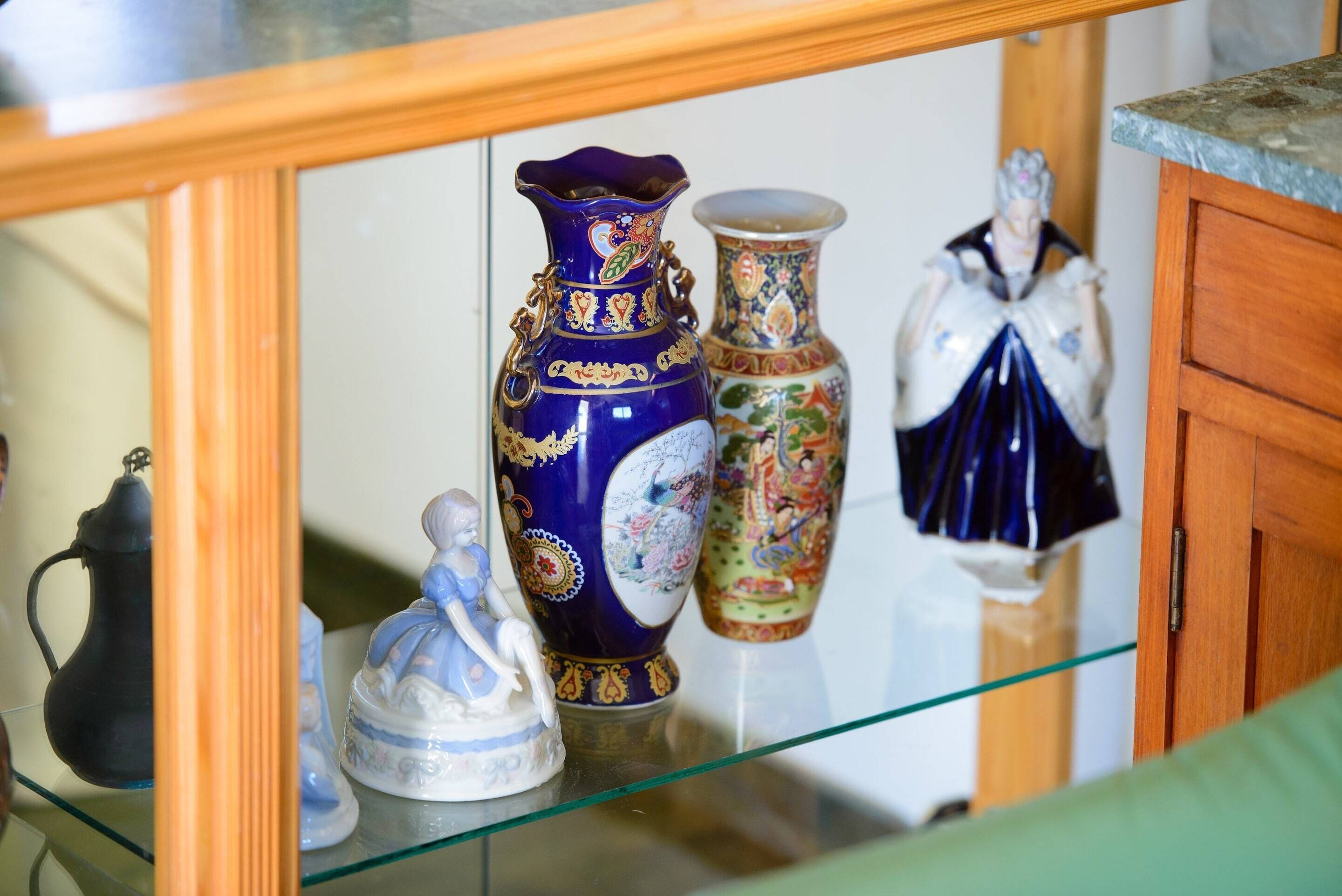 Exposição de vasos e figurines de cerâmica numa prateleira de vidro.